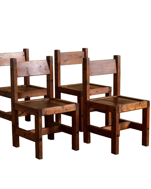 Set of four wooden chairs with slatted seats and backs on a wooden floor.