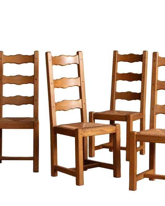 Set of wooden chairs with woven seats against a beige wall.