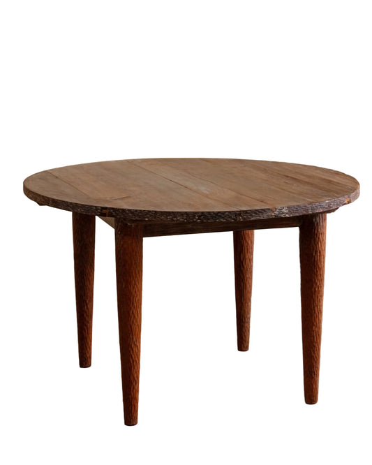 Wooden round table with four legs on a wooden floor against a beige wall