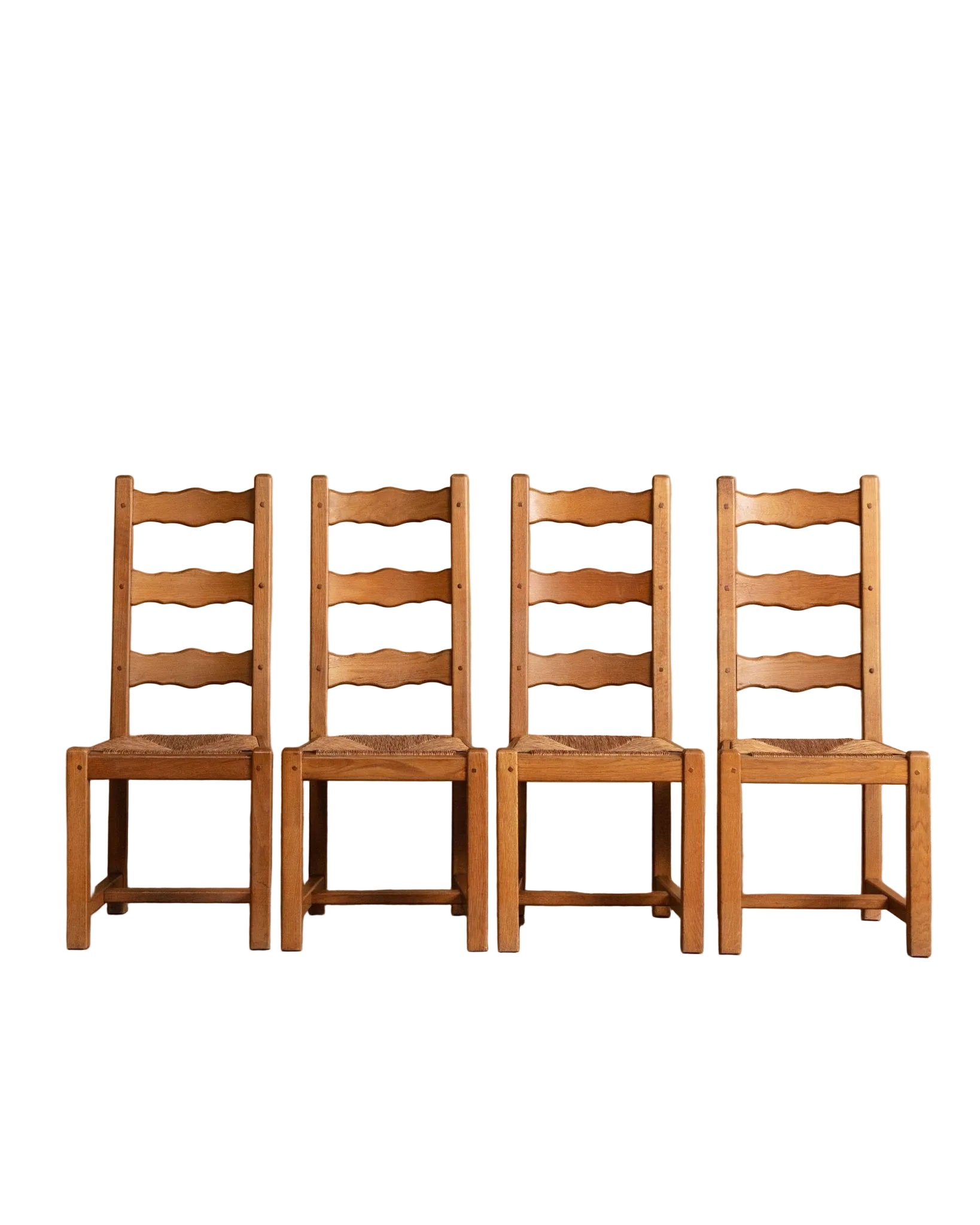 Four wooden chairs with ladder-back design against a beige wall.