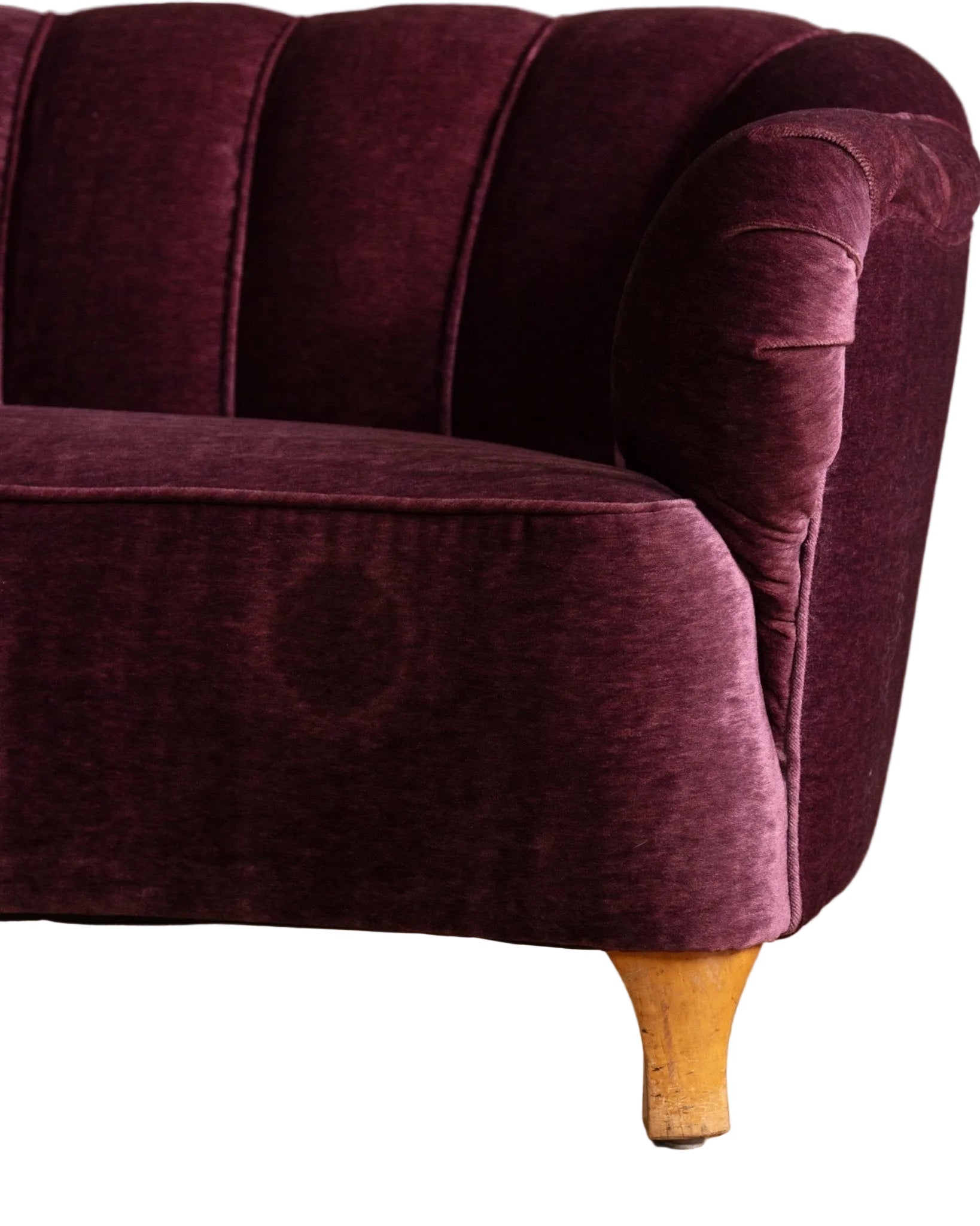 Close-up of a purple velvet sofa with wooden legs on a wooden floor.